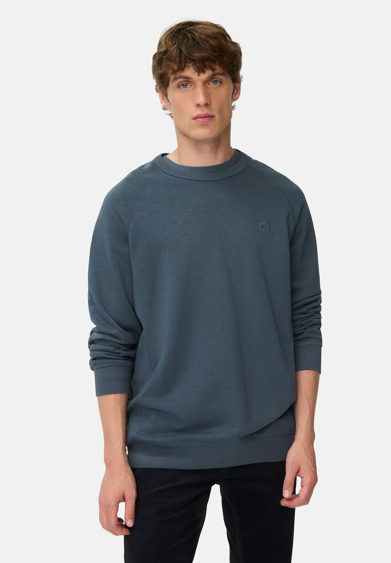 Ciemnoniebieska bluzka z długim rękawem, okrągłym dekoltem i strukturalnym materiałem. Zawiera małe logo na klatce piersiowej oraz ściągacze przy rękawach.