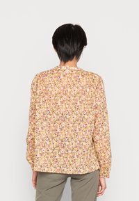 Blusa a maniche lunghe con stampa floreale gialla e motivo denso di fiori rosa e viola. Presenta maniche arricciate e collo rotondo.