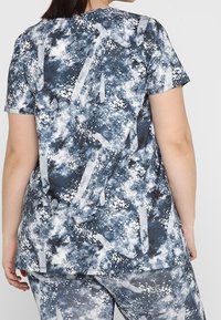 Top de manga corta, azul y gris con un patrón de formas abstractas y motas, confeccionado en una suave tela texturizada, con un corte holgado y un dobladillo redondeado.