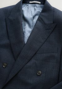 Blazer blu navy doppiopetto in tessuto testurizzato, con foderatura azzurra a pois e due bottoni scuri sul davanti.