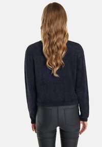 Dunkelblauer, fusseliger Strickpullover mit lockerer Passform und geripptem Saum, kombiniert mit schwarzen, figurbetonten Hosen mit zwei Gesäßtaschen.
