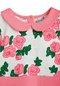 Rosa klänning med blommönster och ljusrosa krage, med gröna blad på en vit bakgrund. Knappar bak. Mjuk tyg.