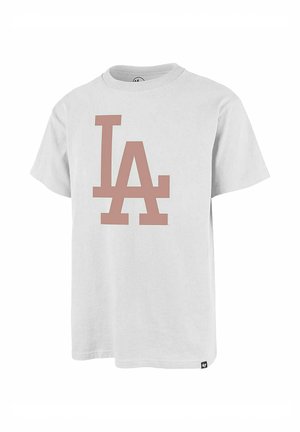 Camiseta blanca de manga corta con grandes letras "LA" en rosa apagado en la parte delantera y una pequeña etiqueta de la marca cerca del dobladillo inferior.