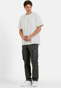 Camiseta de algodón gris con mangas cortas y texto rojo, combinada con pantalones cargo verde oscuro que cuentan con múltiples bolsillos y zapatillas blancas.
