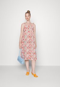 Vestido floral com fundo rosa, alças ajustáveis e cintura franzida. Combinado com uma bolsa azul clara e sapatos amarelos de salto aberto.