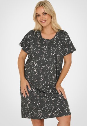 Lächelnde Frau mit blondem Haar, die ein dunkelgraues Kurzarmkleid trägt, das mit verstreuten weißen und rosa Sternmustern verziert ist.