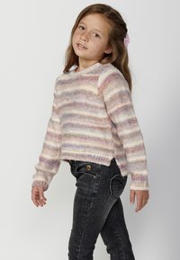 Pull en tricot avec des rayures pastel dans des tons de rose, violet et crème. Il a un col rond et des poignets côtelés, associé à un jean en denim foncé.