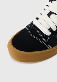 Μαύρο σουέντ αθλητικό παπούτσι με λευκά κορδόνια, αντιθετική ραφή και υφή στη σόλα από καουτσούκ σε χρώμα μέλι. Στρ ογγυλή μύτη και χαμηλό σχέδιο.