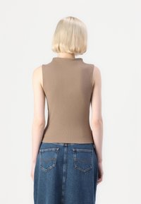 Rjav rebrast brezrokavnik z visokim ovratnikom, v kombinaciji z jeans krilom, ki ima dve zadnji žepki in rahlo razširitev na robu.