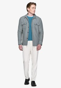 Rutig skjortejakke i blå, grøn og hvid, parret med en teal strikket sweater, creme farvede bukser med snor og sorte sko.