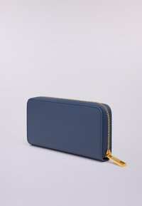 Portafoglio blu in pelle con zip a tutto giro, finitura testurizzata e zip dorata, posato su una superficie grigio chiaro.