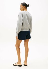 Felpa grigia con maniche a palloncino, pantaloni corti blu navy e sandali neutri. Tessuto morbido, design casual e vita aderente.