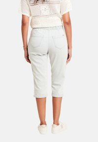 Lichtblauwe cropped jeans met elastische tailleband, opgerolde mouwen en twee achterzakken. Gemaakt met witte sneakers en een opengehaakte top.