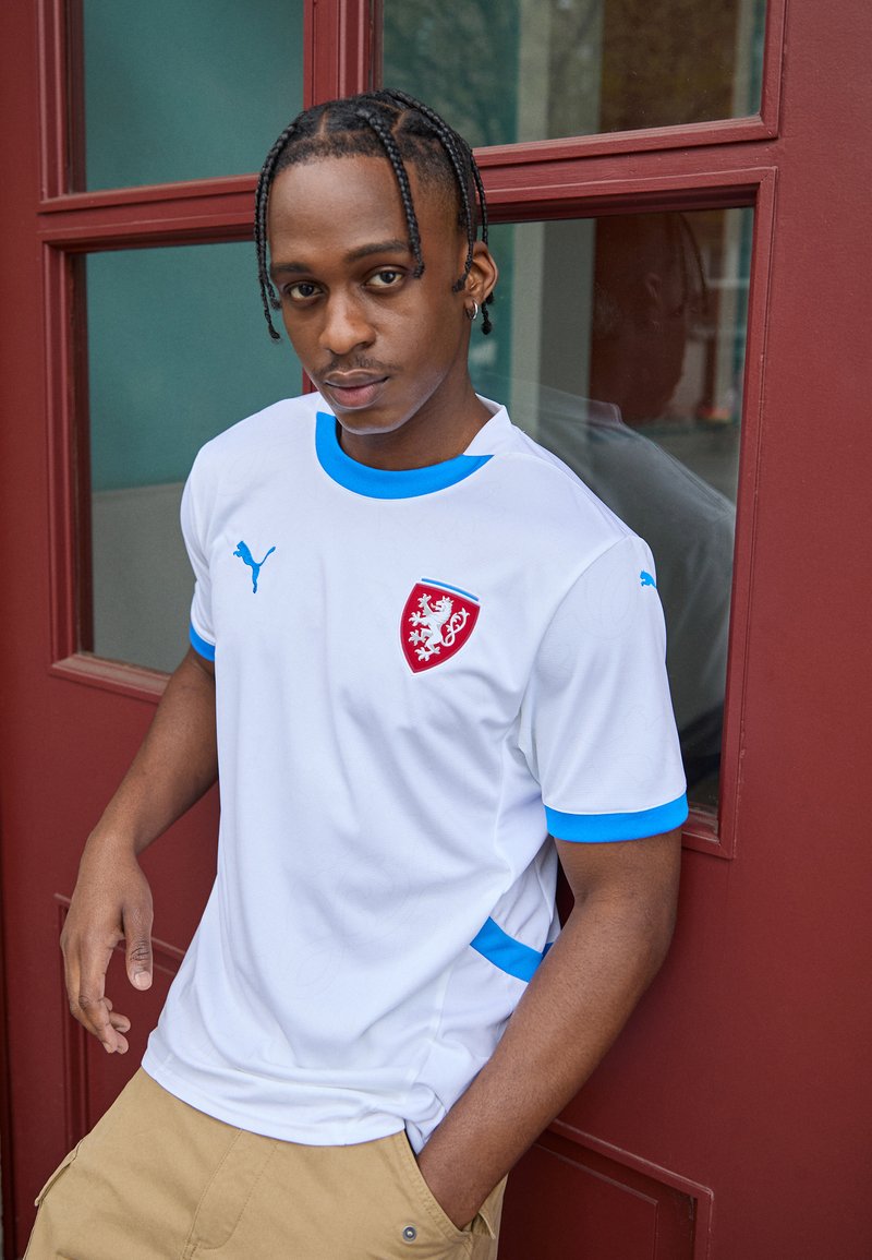 Balts sporta krekls ar ziliem akcentiem, ar sarkano emblēmu, apaļu kakla izgriezumu un īsām piedurknēm. Valkāts kopā ar khaki krāsas šortiem.