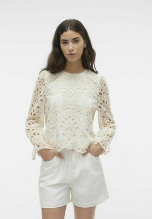 Hvit brodert bluse med blomsterutskjæringer og lange, vidde ermer. Har rund halslinning og bølget kant.
