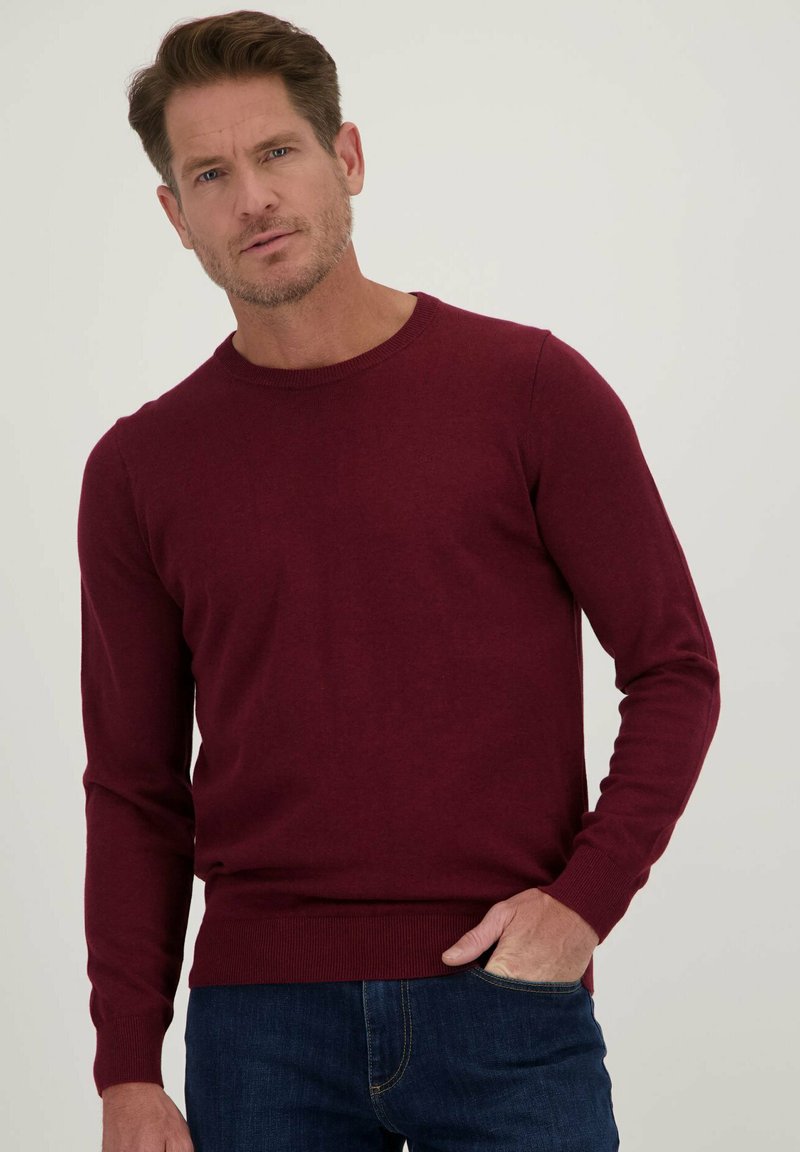 Bordeaux gebreide trui met een ronde hals en lange mouwen, voorzien van ribgebreide manchetten en onderrand, gedragen over donkerblauwe jeans.