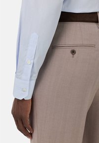 Camicetta a righe blu chiaro con polsini bottonati e pantaloni beige chiaro texture con tasca posteriore dotata di bottone.