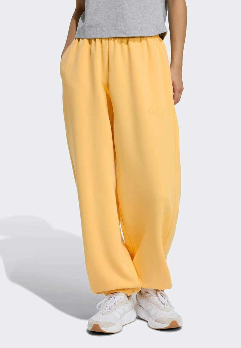 Žlté tepláky s elastickým pásom, vo voľnom strihu, a bočnými vreckami, skombinované s bielymi teniskami s jemnými akcentmi a textúrovanými podrážkami.