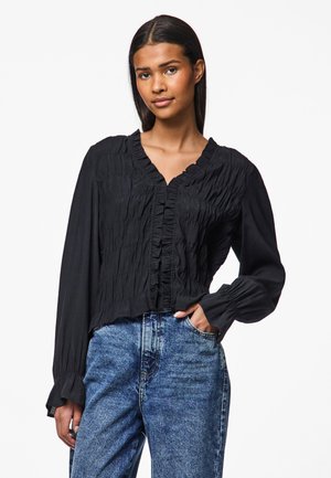 Black blouse with ruffled front and neckline, long sleeves with gathered cuffs, made from lightweight fabric, styled with high-waisted jeans.