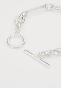 Silver chain bracelet featuring rounded links, a circular charm, and a horizontal bar clasp with engraved detailing. Smooth, polished surface.