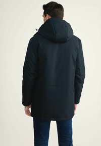 Czarna zimowa kurtka z kapturem, z zamkiem błyskawicznym i bocznymi kieszeniami. Gładki materiał z subtelnymi detalami w postaci przeszyć; średniej długości krój.