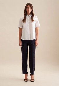 Biała koszula na guziki z krótkim rękawem; zestawiona z dopasowanymi granatowymi spodniami; noszona z czarnymi sandałami na obcasie; minimalistyczny design i czyste linie.