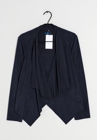 Chaqueta ligera de color azul marino con diseño de frente drapeado, mangas largas y sutil textura. Etiqueta y percha visibles.