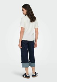 Cremefarvet bomulds t-shirt med korte ærmer, parret med mørkeblå opsmøgede jeans og marineblå sneakers med hvide detaljer.