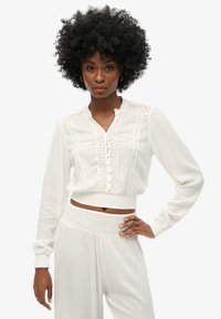 Witte, cropped blouse met lange mouwen, kantdetails en knoopsluiting. Lichtgewicht stof met een zachte textuur en een aansluitende tailleband.