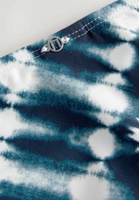Material textil cu motive albastre și albe, având o textură moale, cu un accent oval din metal argintiu și cusături albe pe margine.