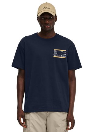 Granatowy t-shirt z krótkim rękawem wykonany z bawełny, z kieszonkowym nadrukiem w odcieniu beżowym, z tekstem i logo na przodzie.