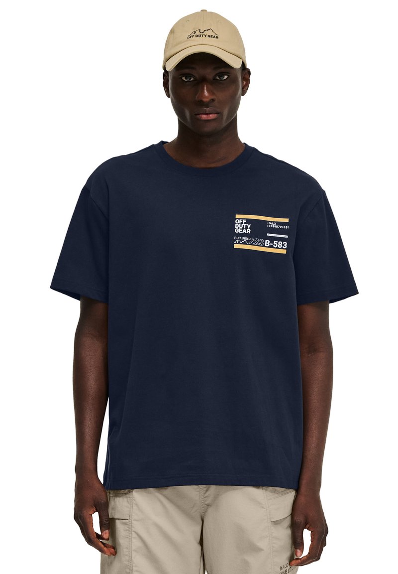 Donkerblauwe t-shirt met korte mouwen van katoen, met een grafisch ontwerp op de borstzak in beige, met tekst en een logo op de voorkant.