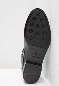 Semelle de chaussure synthétique noire avec des motifs de grip circulaires, un design lisse, une étiquette de taille 37 et une surface texturée pour une meilleure adhérence.