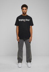 Sort bomulds t-shirt med "glemte ansigtter" grafik i hvid, parret med grå rummelige jeans og hvide sneakers. Enkelt design, afslappet pasform.