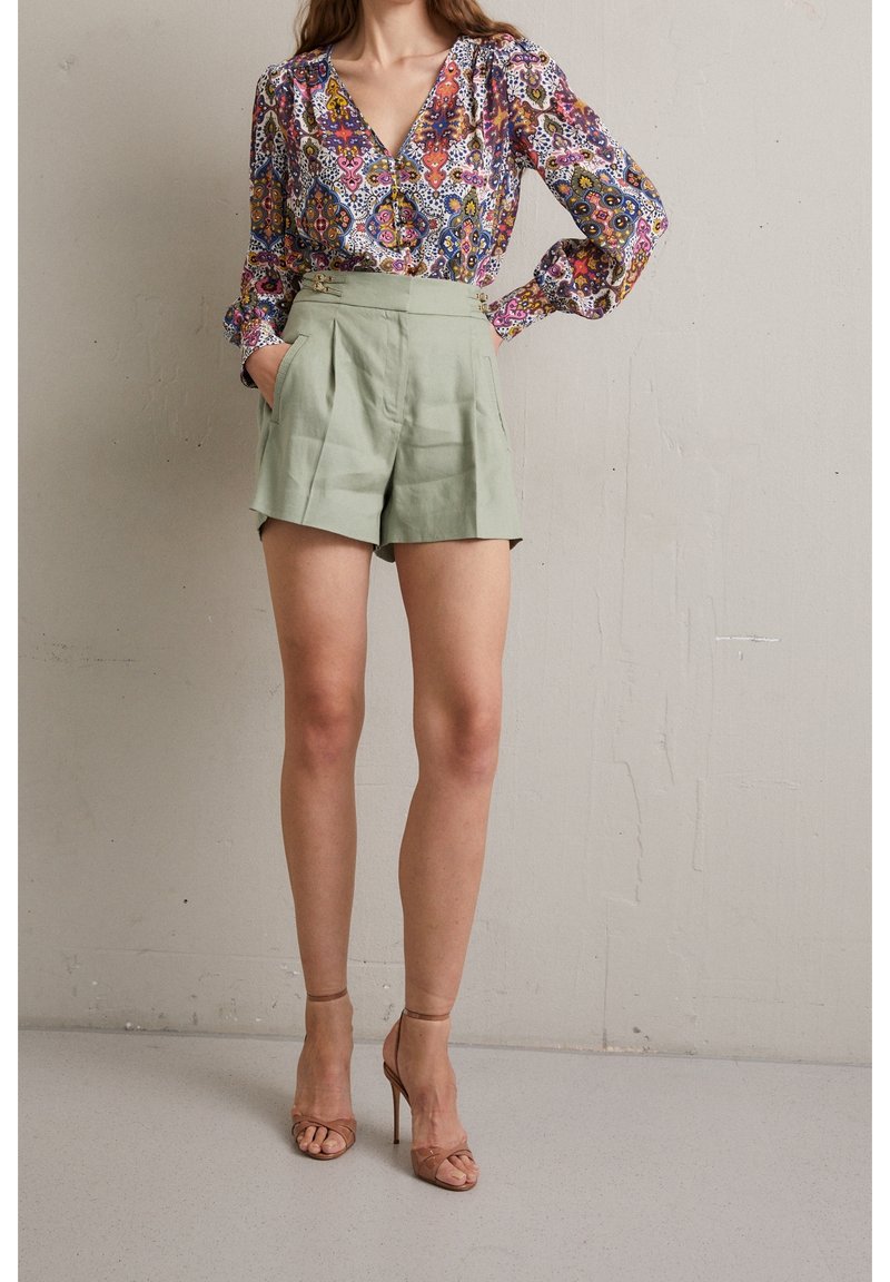 Multicolore bloemenblouse met een diepe V-hals en wijdvallende mouwen, gecombineerd met lichtgroene high-waisted shorts met plooien en zakken.