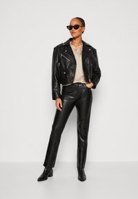 Veste de moto en cuir noir avec des zips argentés, associée à un pantalon en cuir noir ajusté. Portée avec un chemisier léger et des bottines.