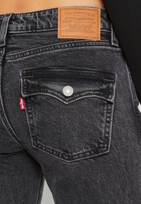 Vaqueros de mezclilla negra con un diseño clásico de 5 bolsillos y costuras blancas contrastantes. Presenta una parche de cuero y una etiqueta roja de Levi's en el bolsillo trasero.