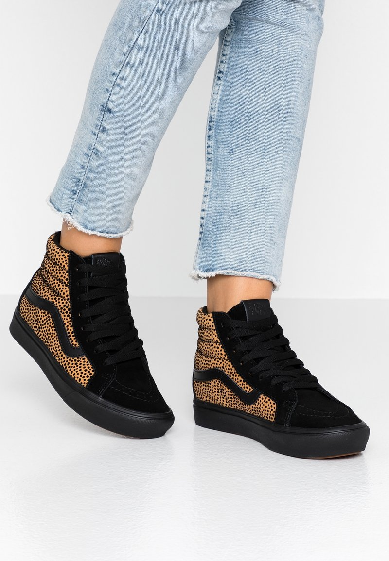 Pieds portant des baskets montantes avec des panneaux imprimé léopard noir et fauve, associées à un jean bleu clair court à ourlet effiloché.