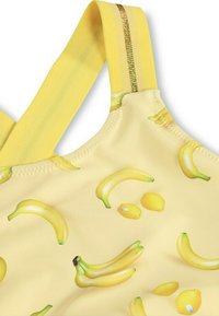 Gul baddräkt med ett mönster av bananer och citroner, med gula axelband och en gyllene detalj. Slät textur, livliga färger.