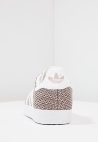 Bruna vävda sneakers med vita accenter, som har tre vita ränder, en texturerad sula och en logotyp på hälen.