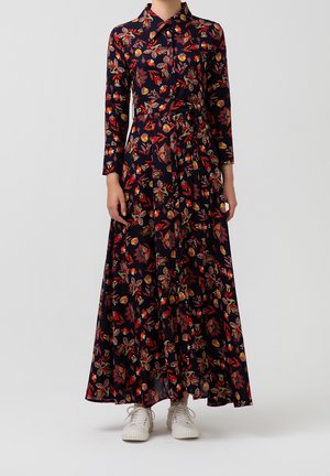 Marineblaues Maxikleid mit langen Ärmeln, buntem Blumenmuster, Knopfleiste vorne, Taillengürtel, getragen mit weißen Sneakern.