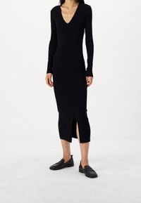 Svart ribbad stickad klänning med långa ärmar, V-ringning och sidospår. Matchad med svarta platta skor. Minimalistisk design och figurnära siluett.