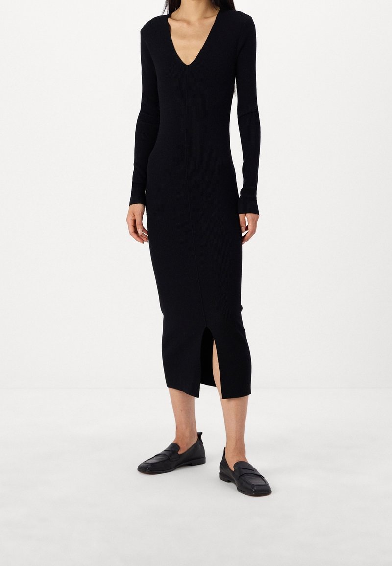 Svart ribbad stickad klänning med långa ärmar, V-ringning och sidospår. Matchad med svarta platta skor. Minimalistisk design och figurnära siluett.