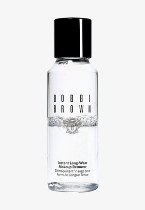 Heldere vloeibare make-up remover in een cilindrische fles met een zwarte dop. Bevat zwarte tekst en een decoratief zilveren logo op het etiket.