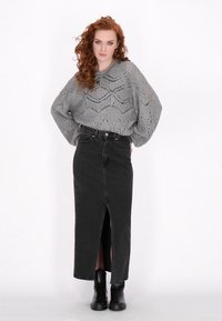 Lichtgrijze gebreide trui met een opengewerkt patroon, gecombineerd met een hoogwaist zwarte denim rok met een voorknijp en zwarte enkellaarzen.