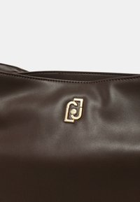 Borsa a tracolla in pelle marrone caratterizzata da una texture liscia, un accento in logo dorato e un design elegante. La borsa ha una chiusura a zip nella parte superiore.