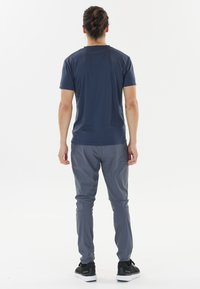 Marineblaue Kurzarm-T-Shirts kombiniert mit hellgrauen Hosen. Beide Kleidungsstücke haben ein elegantes, sportliches Design und minimalistischen Stil. Sichtbare schwarze Sneakers.