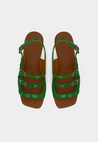 Sandales en cuir verni vert avec trois brides ajustables et boucles argentées. Semelle marron texturée offrant adhérence et confort.