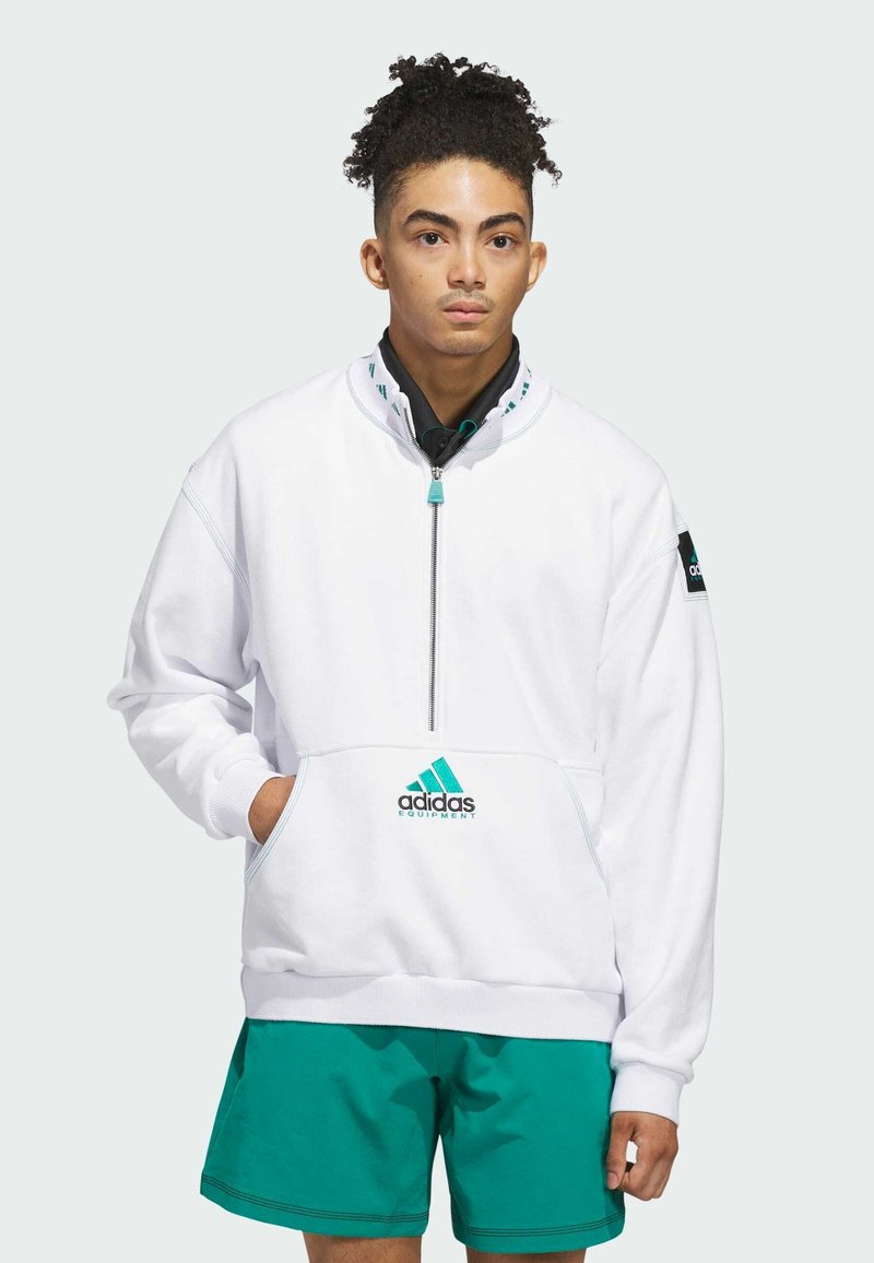 Felpa bianca con colletto a metà zip e tasca frontale, caratterizzata dal logo adidas e dettagli in teal. Abbinata a pantaloni corti teal.