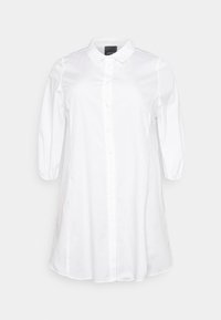 Valkoinen napilla varustettu paita, jossa on klassinen kaulus, kolmanneksi puolipitkät hihat ja hieman väljä istuvuus. Tasainen, kudottu kangas, jossa on hieno kiilto.